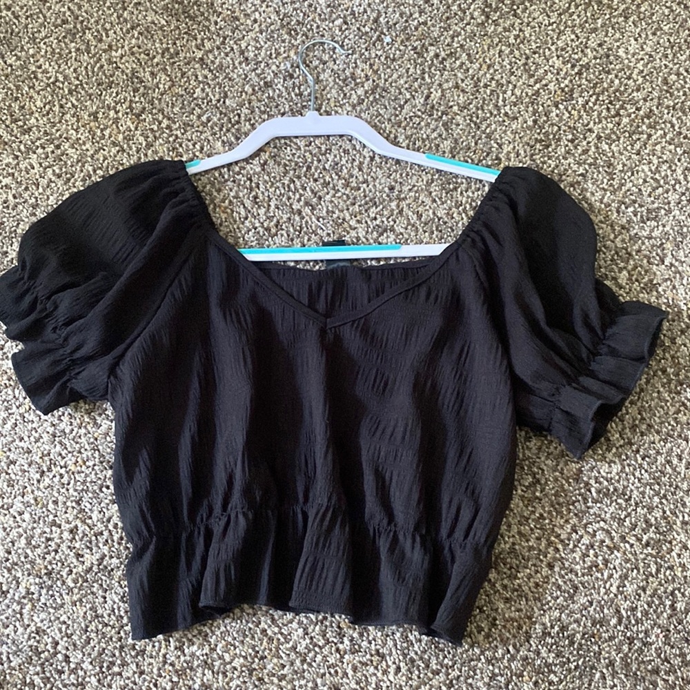 This is a cropped top that is a solid black, with a ruffle, flared sleeve.